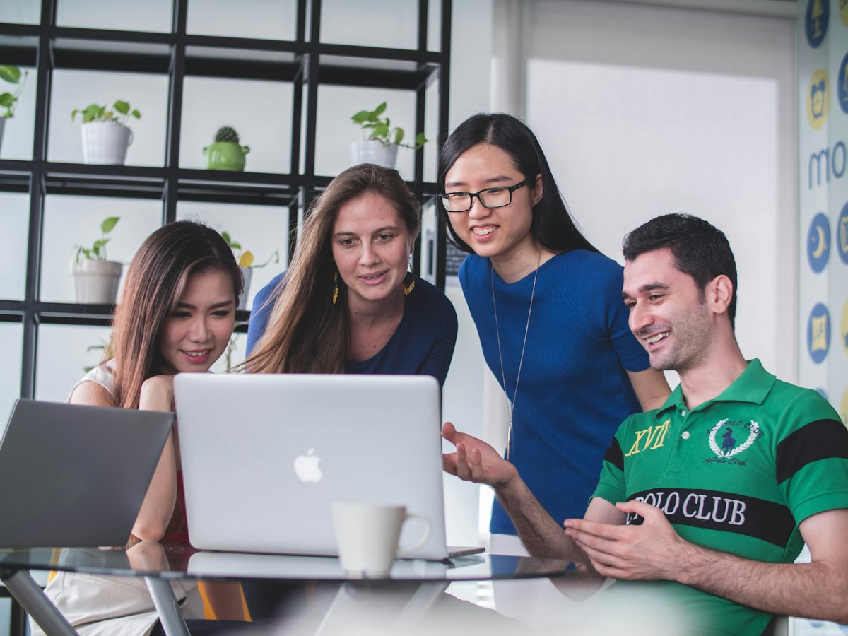 Four colleagues smiling while looking at a laptop together